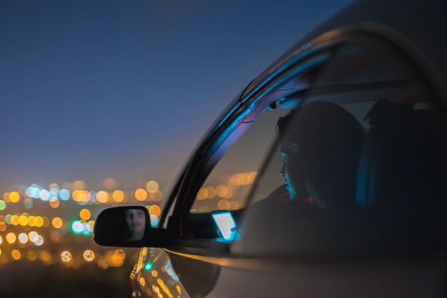 The attractive woman phone in the car on the background of the city. night time