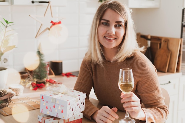 Attractive woman sitting in the kitchen with christmas gifts and glass of champagne