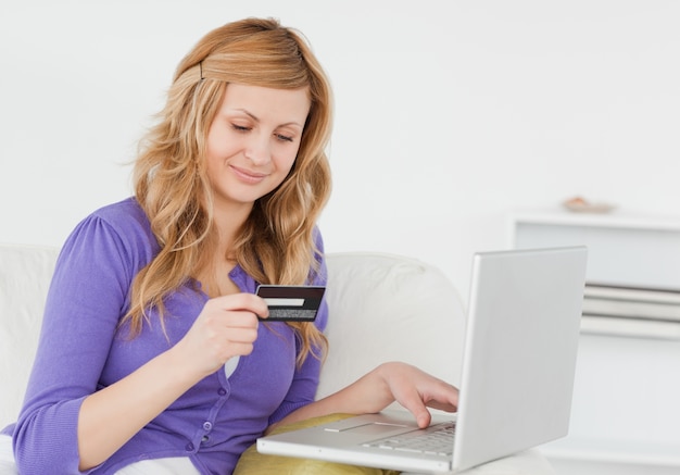 Attractive woman sitting on a sofa is going to make a payment on the internet