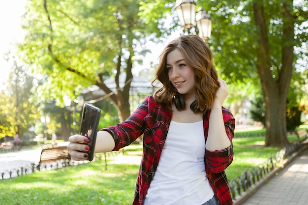 Attractive woman student makes selfie on a smartphone in a city park.