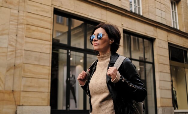 Attractive woman in sunglasses walks in city with backpack female tourist looking around