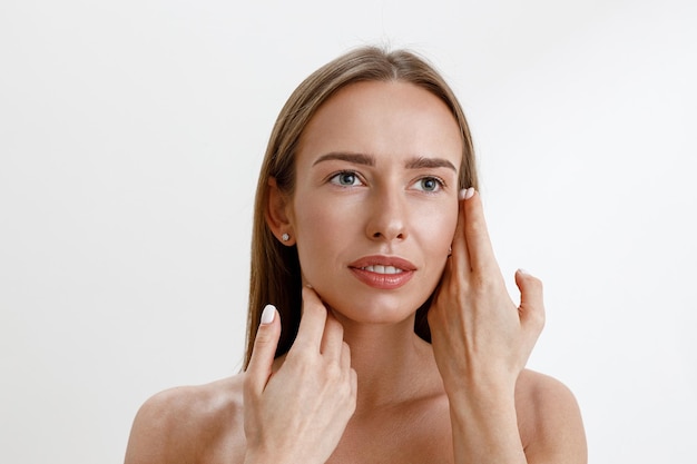 Attractive woman touching her perfect face over white studio background healthcare routine concept