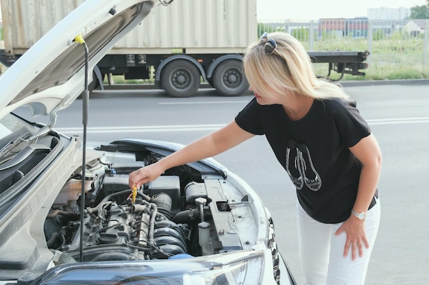 Attractive woman with long blond hair takes out a dipstick for oil from a car engine