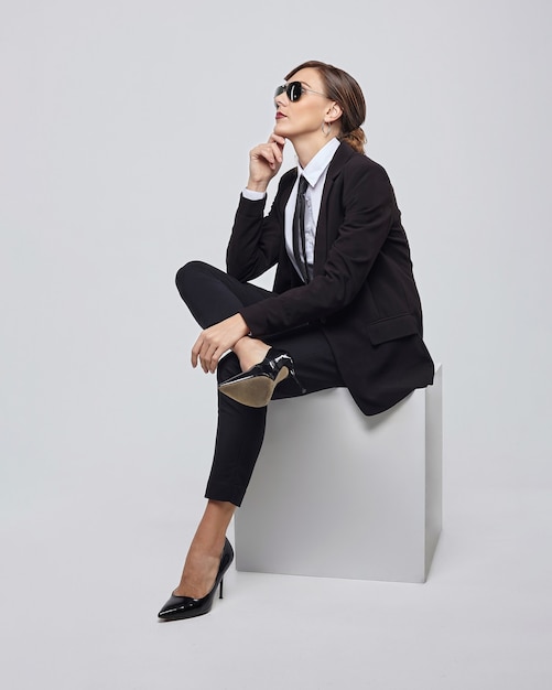 Attractive woman with a retro hairstyle poses in a men's suit and sunglasses