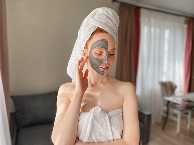 Attractive woman with a towel on her head and a clay mask