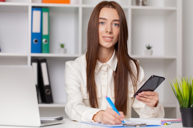 Attractive woman working on smart phone in her workstation.