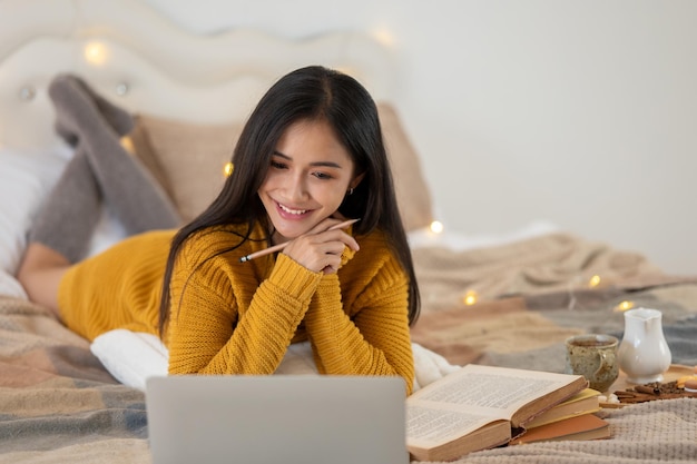 An attractive young Asian female college student is doing homework on her bed in her bedroom