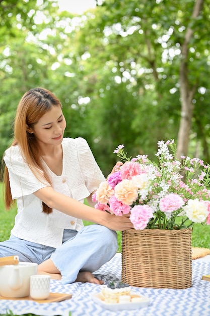 Attractive young Asian female picnicking in the garden holding a flower basket