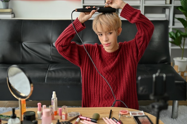 An attractive young Asian gay beauty influencer using a straightener to curl his hair