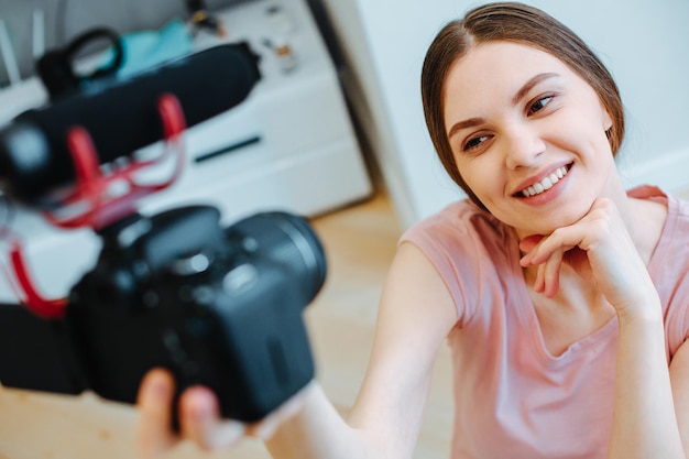 Photo attractive young blogger holding a camera with microphone and touching her chin while smiling