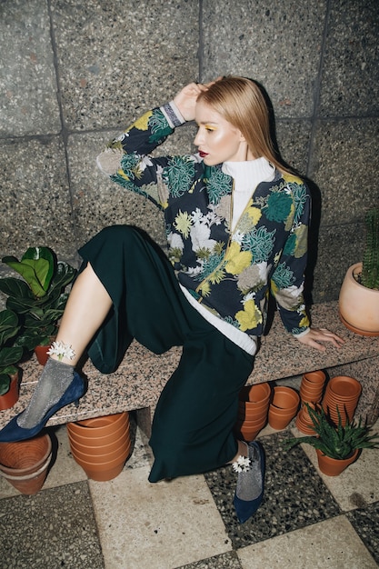 Photo attractive young blond woman posing in the flower boutique in a stylish dress with tropical print