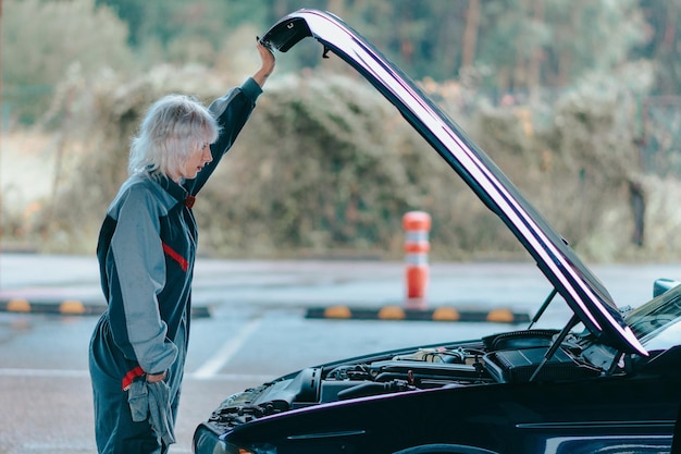 Attractive young blonde female wearing an auto mechanic uniform and repairing the car