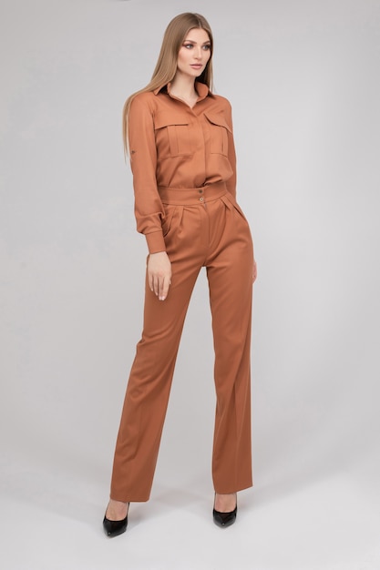 Attractive young blonde model with perfect slim body posing in trendy orange pantsuit full length. Beautiful fashion girl standing in stylish classic clothing isolated on white studio background