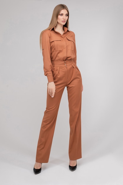 Attractive young blonde model with perfect slim body posing in trendy orange pantsuit full length