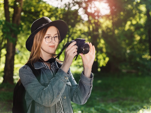 Attractive young girl in a hat makes photo on camera outdoors