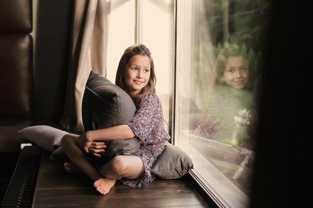 Attractive young girl near the window in a blue dress