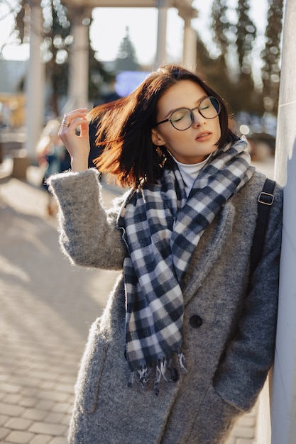 Attractive young girl wearing glasses in a coat walking on a sunny day