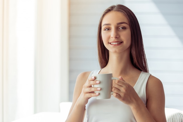 Attractive young girl in white singlet is holding a cup.