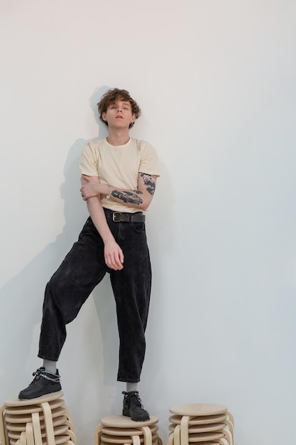 Attractive young guy standing on the top of stools by the white wall