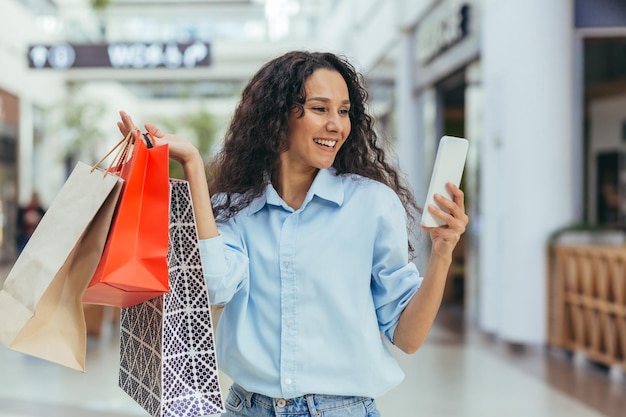 An attractive young latin american woman is shopping in a shopping center holding colorful bags in