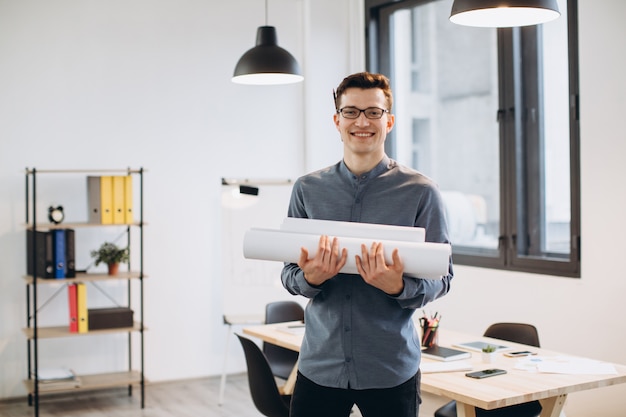 Attractive young man architect in glasses standing isolated over loft office, carrying drawings, holding house scheme