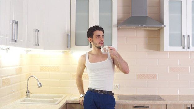 Attractive young man drinking water from a glass in kitchen at home