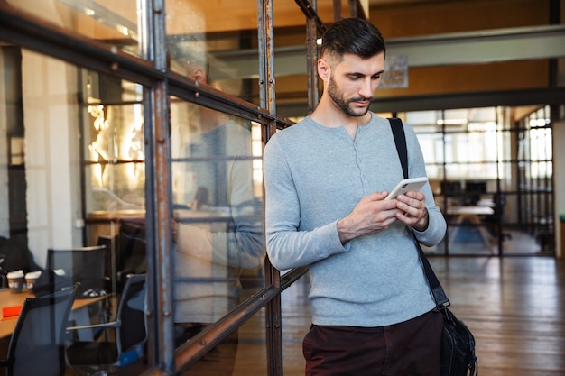 Attractive young man standing in the hub, using mobile phone