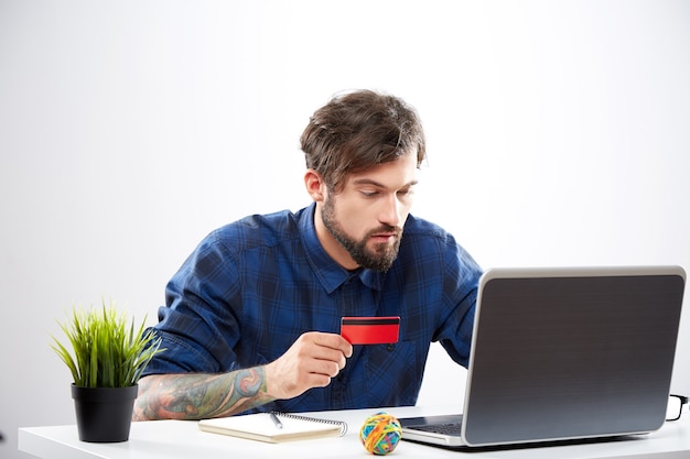 Attractive young man wearing blue shirt sitting with laptop, online shopping concept, portrait, mobile online shopping.