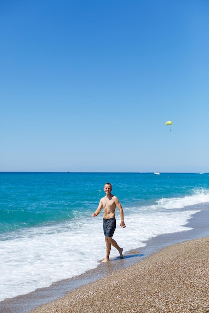 Attractive young man with a beautiful body in shorts walks along the sandy seashore and enjoying summer vacation