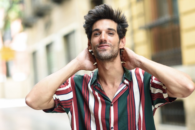 Attractive young man with dark hair and modern hairstyle wearing casual clothes outdoors