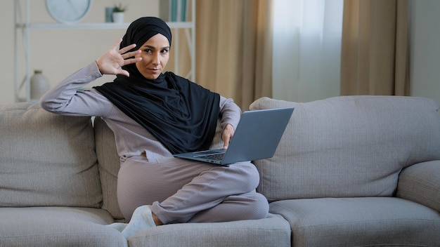 Attractive young muslim woman wear hijab sit on cozy sofa in living room adorable energetic