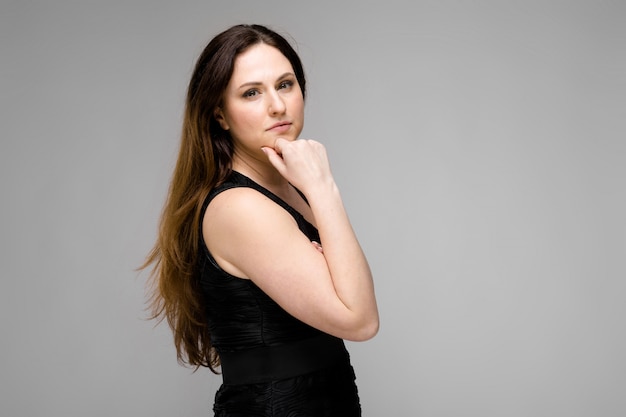 Attractive young positive brunette caucasian smiling business woman in black dress isolated on gray