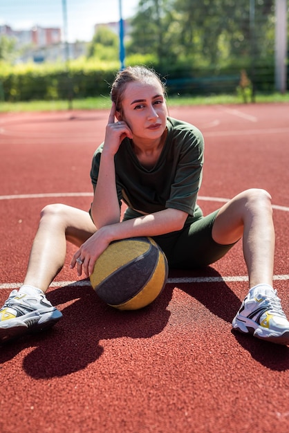 Attractive young slim woman posing sitting on a basketball court holding a basketball