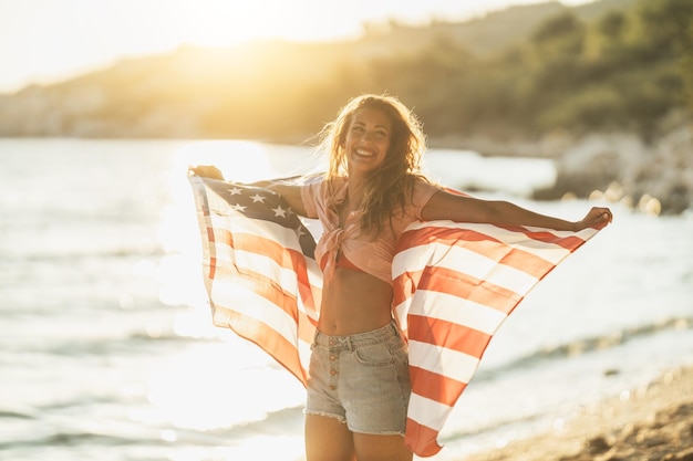 Attractive young smiling woman with American national flag enjoying a relaxing day on the beach.