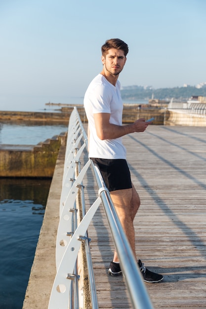 Attractive young sportsman using mobile phone standing outdoors