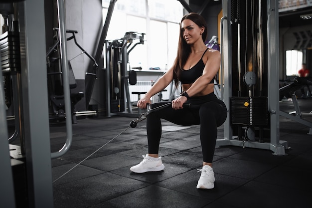 Attractive young sportswoman doing squats in crossover gym machine, copy space