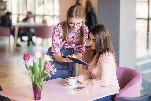 Attractive young waitress using a tablet computer to take an order from a customer in a coffee shop.