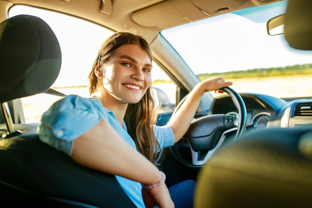 Attractive young woman in blue shirt at sunset light with her car