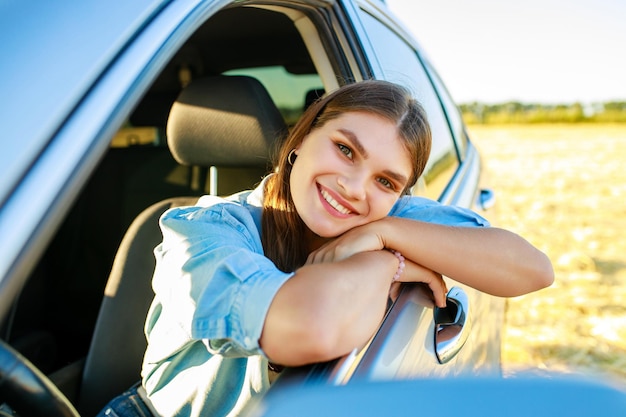 Attractive young woman in blue shirt at sunset light with her car