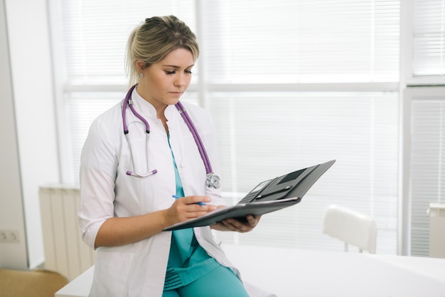 Attractive young woman doctor holding medic clipboard  Handome young woman doctor or nurse in a lab coat and stethoscope standing taking notes on a clipboard