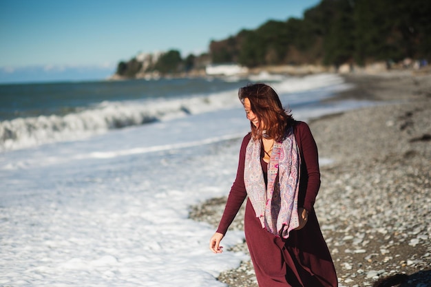 Photo attractive young woman enjoying on a sea wave on the beach cheerful brunette in a burgundy dress and