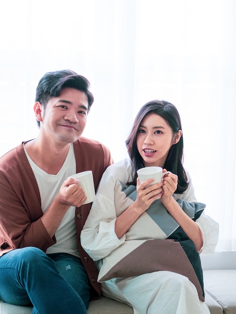 Attractive young woman and handsome man are enjoying spending time together at home with cup of coffee in hands.