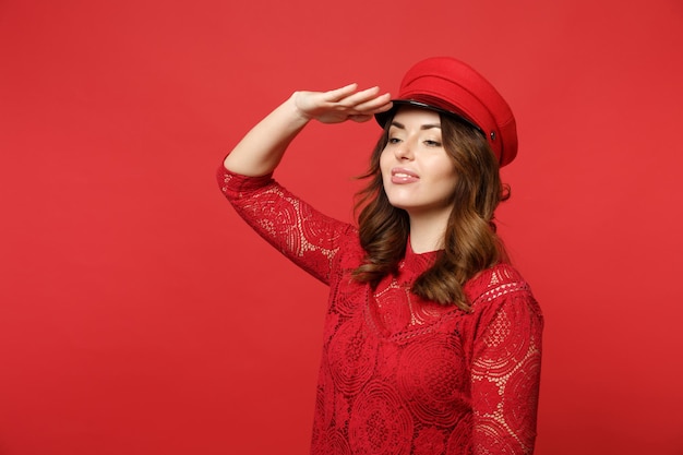 Attractive young woman in lace dress, cap holding hand at forehead looking far away†distance isolated on bright red background in studio. People sincere emotions lifestyle concept. Mock up copy spac