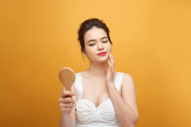 Attractive young woman looking into hand mirror on yellow background