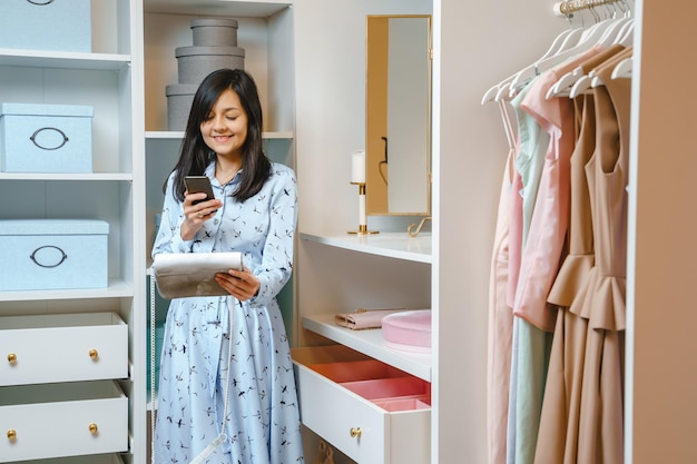 Attractive young woman making photo of handbag on smartphone in dressing room Fashion and style concept