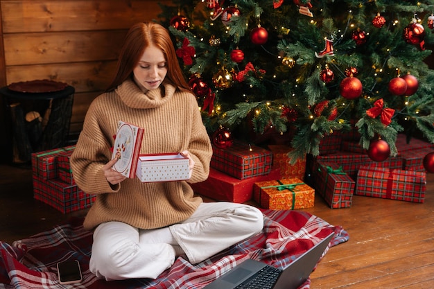 Attractive young woman opening gift box with christmas present on background of xmas tree