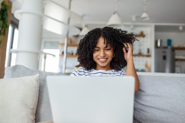 Attractive young woman sitting alone on her sofa at home and using her laptop