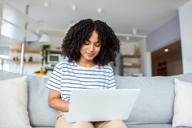 Attractive young woman sitting alone on her sofa at home and using her laptop