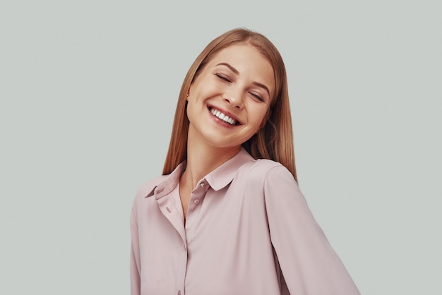 Attractive young woman smiling while standing against grey background