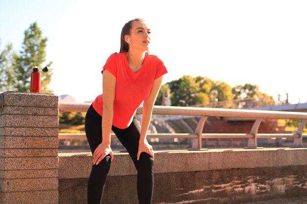 Attractive young woman in sports clothing taking a break while sitting outdoors.